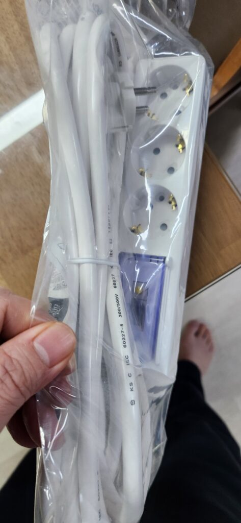 손에 든 비닐 포장 안의 써보니 고용량 3구 멀티탭과 흰색 전선