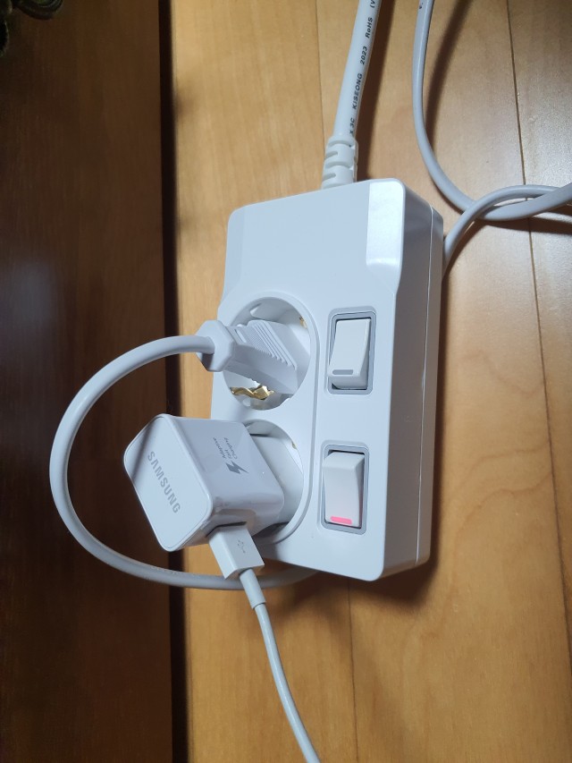 나무 바닥의 개별 스위치형 2구 멀티탭에 연결된 흰 플러그와 USB 충전기